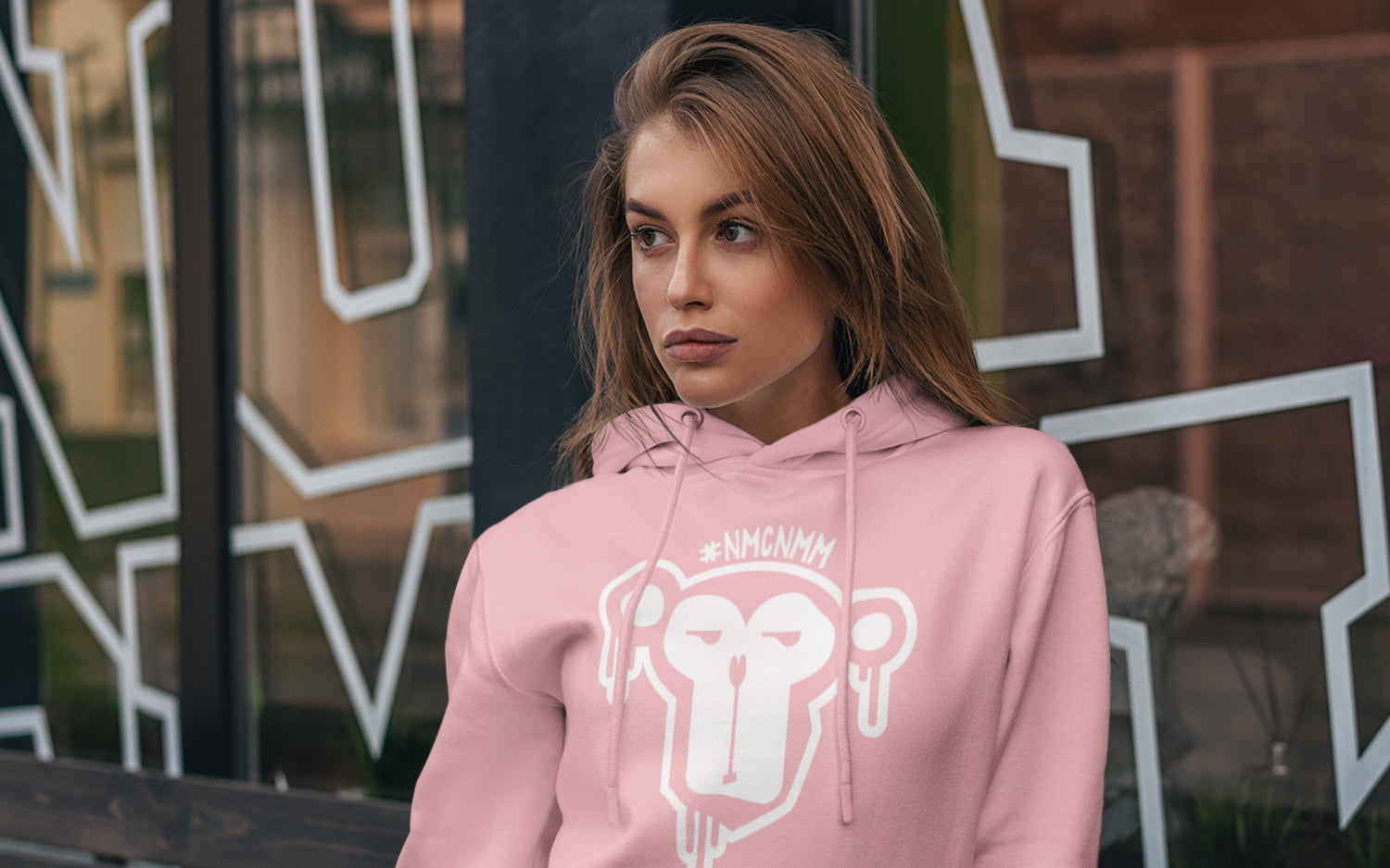 Junge Frau in rosanem Kapuzenpullover mit Affen-Print vor Schaufester