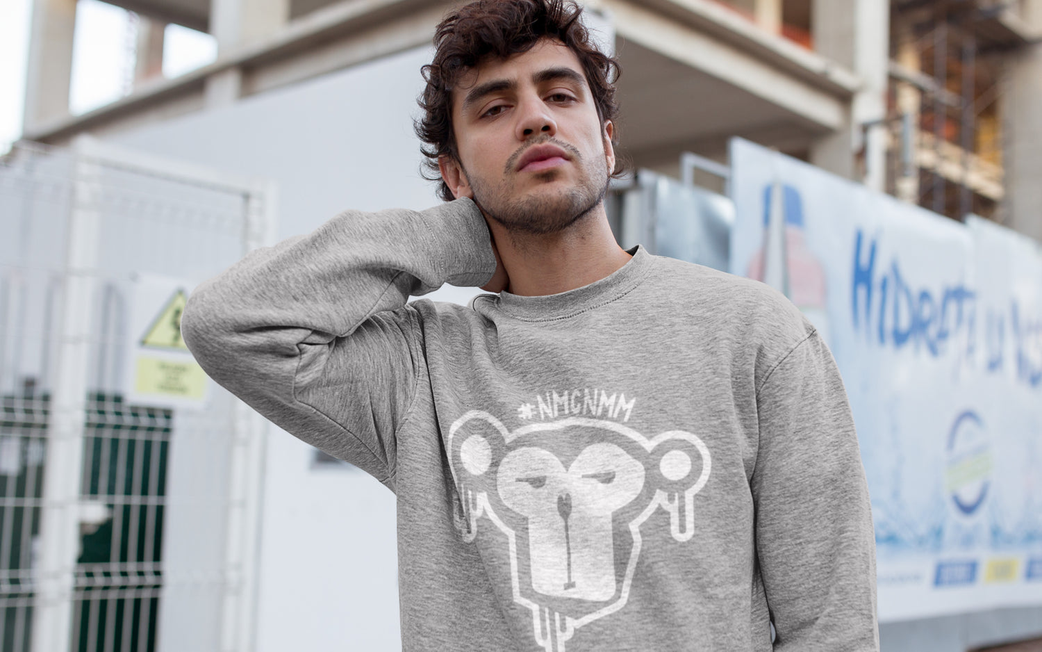 Junger Mann mit grauem Sweatshirt mit Affen-Print vor urbanem Hintergrund